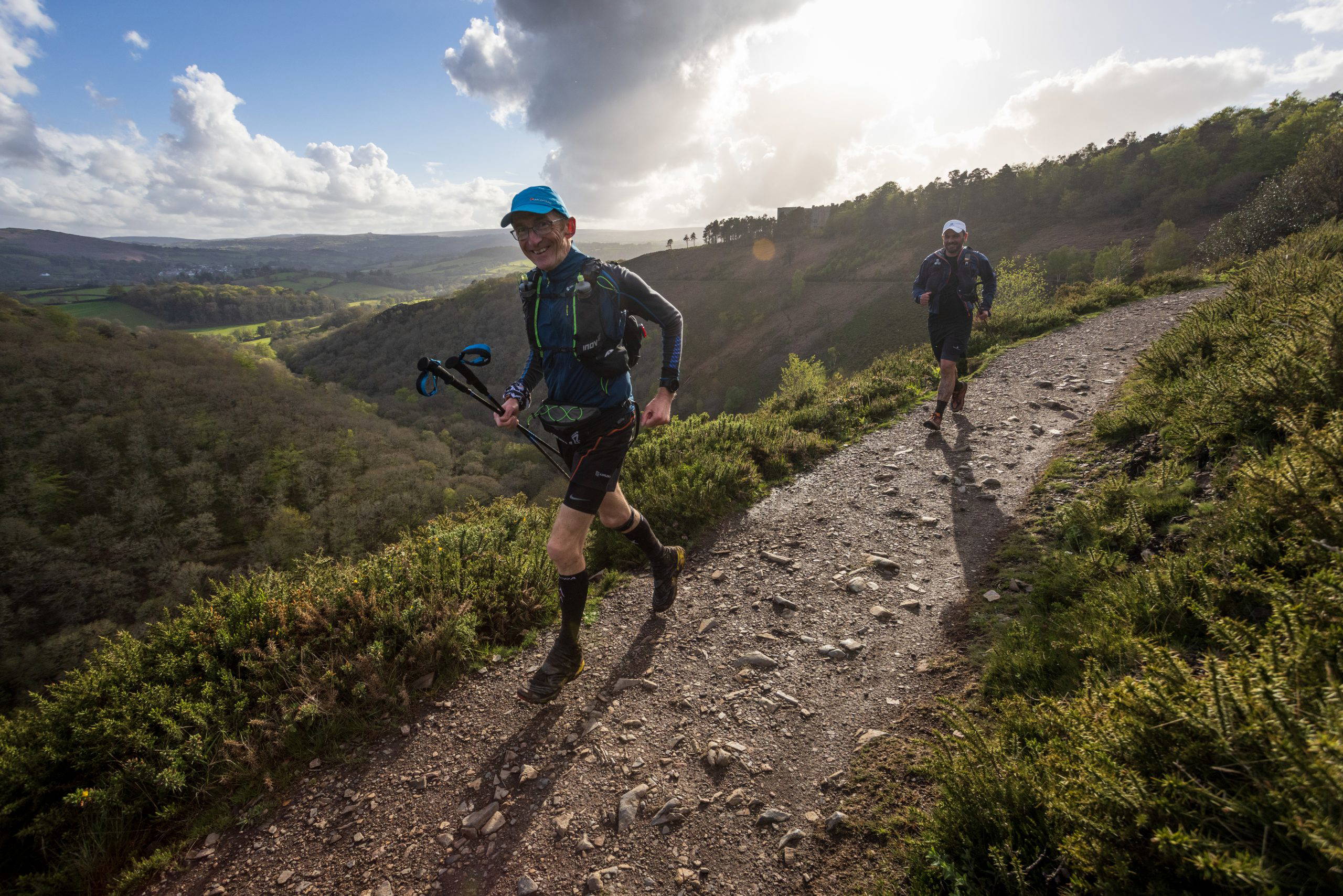 An image of two older individuals hiking a path in the hills