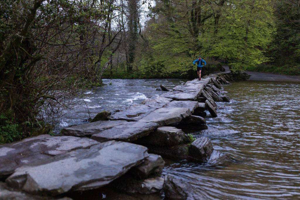 An image of an individual jogging across a stone bridge over a river.