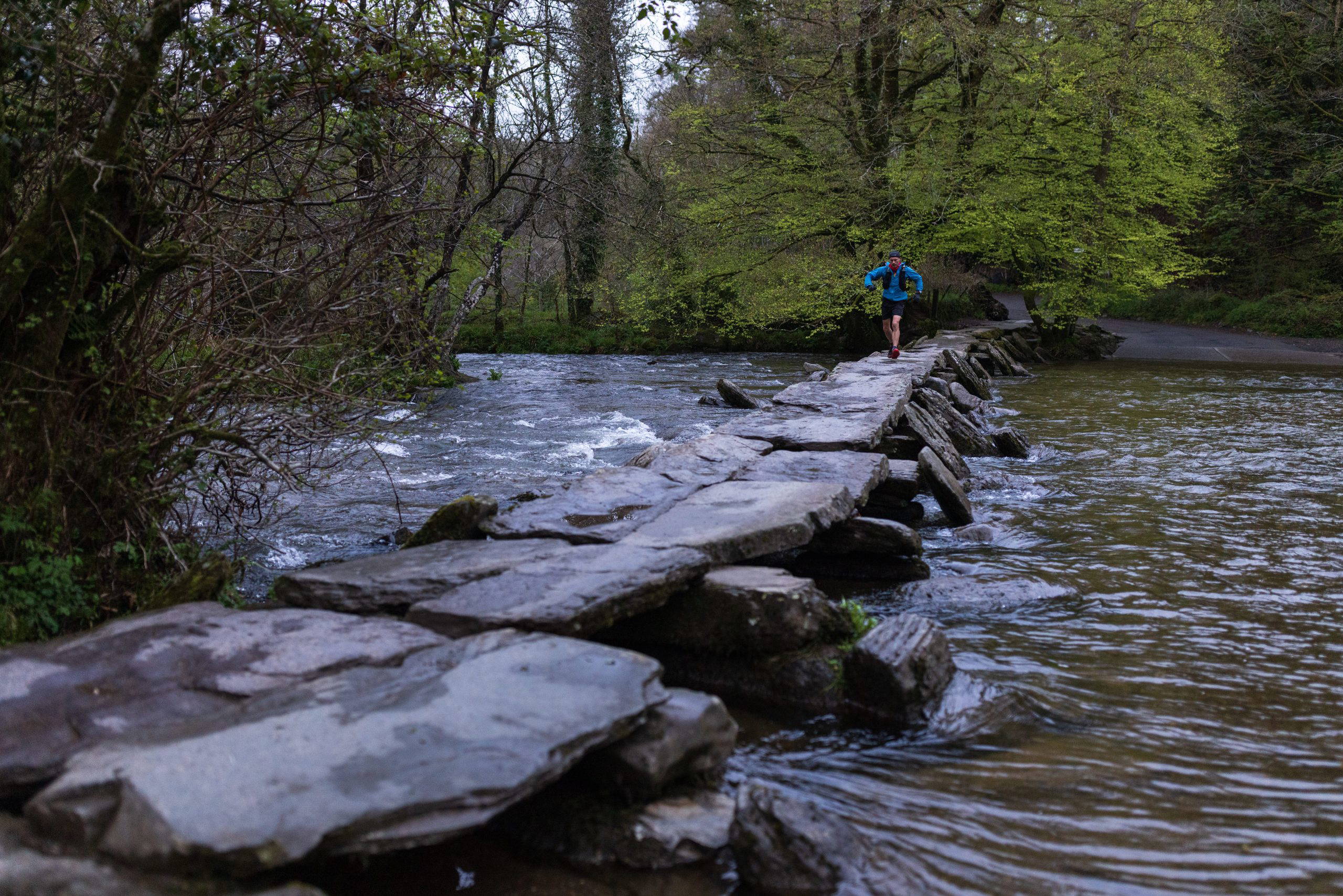 An image of an individual jogging across a stone bridge over a river.