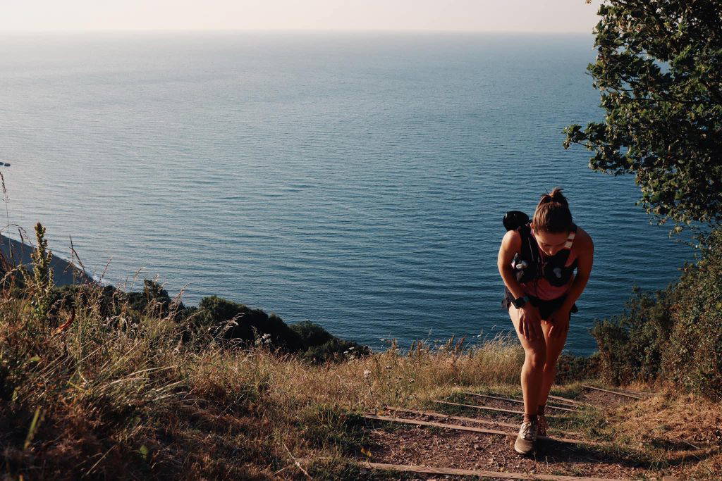 An image of a woman hiking up a trail along the coast.