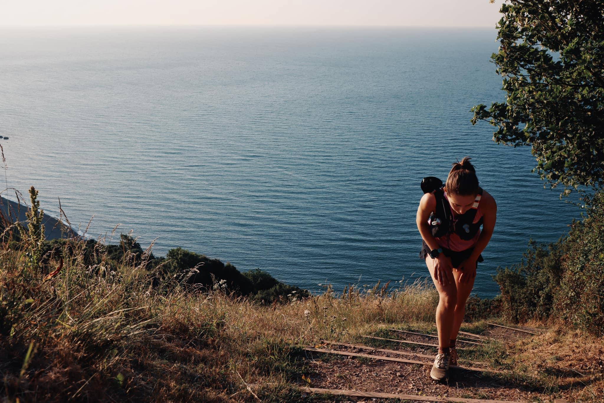 An image of a woman hiking up a trail along the coast.