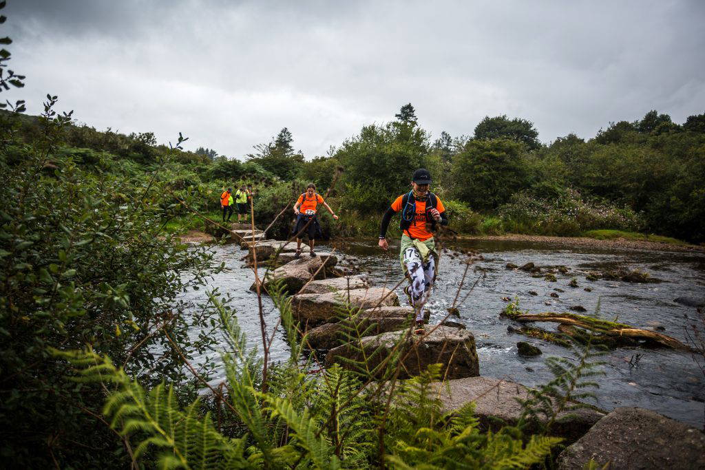 An image of a few hikers traversing over rocks in a river.