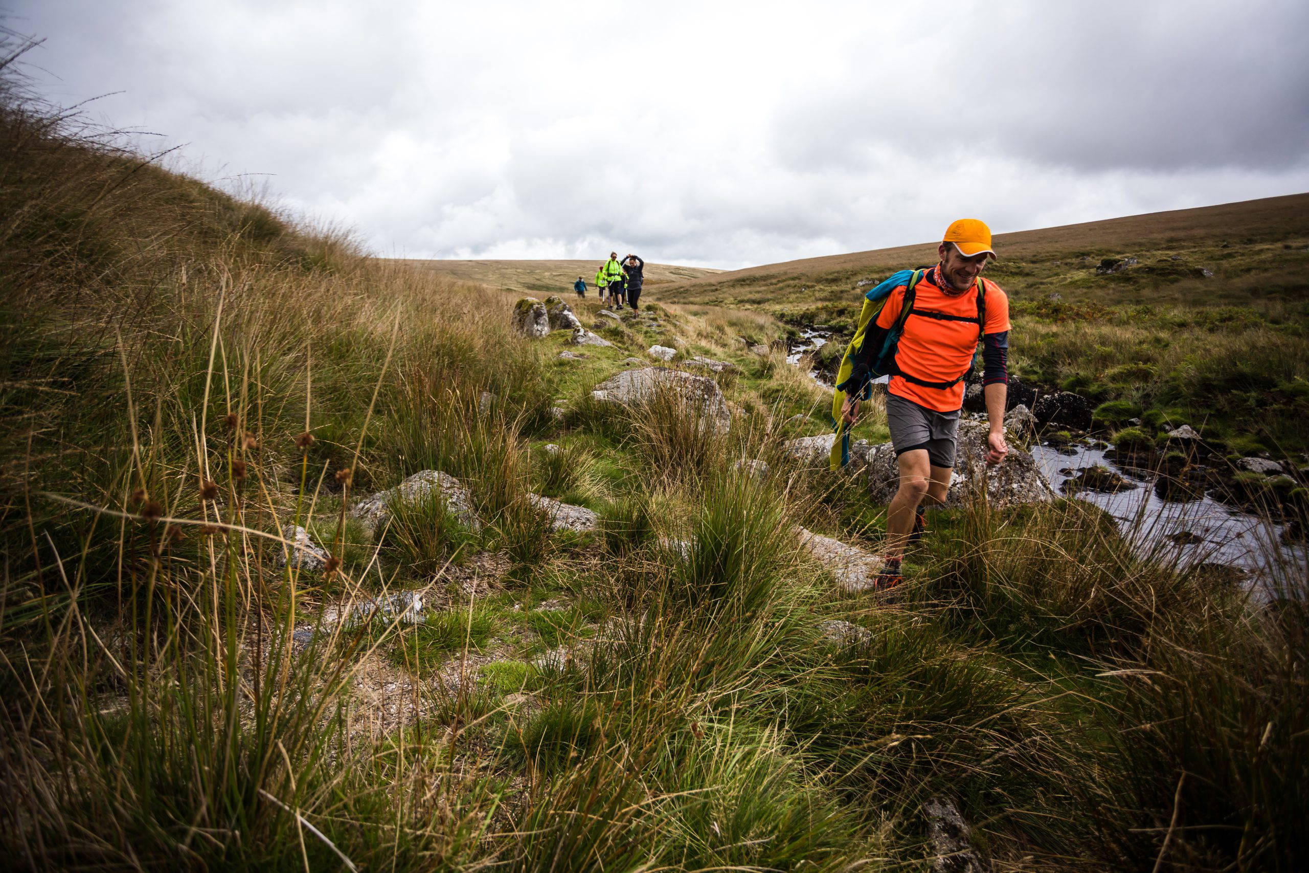 A group of people traversing Dartmoor near a creekside.