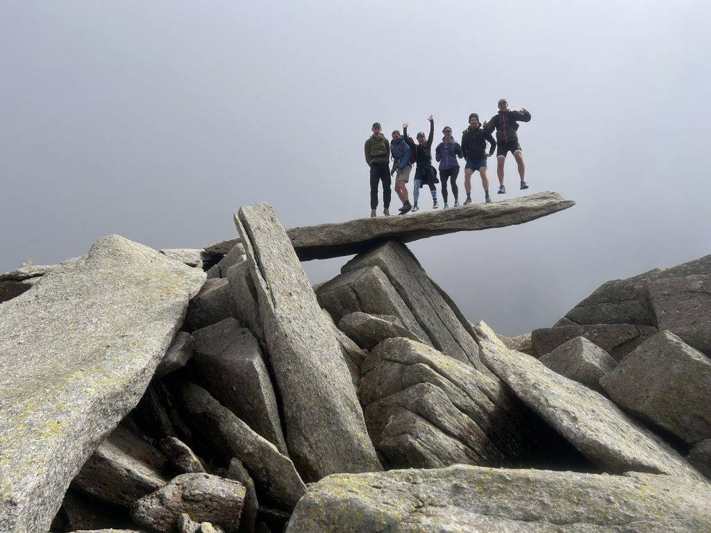 An image of a group of people on top of a balanced boulder.