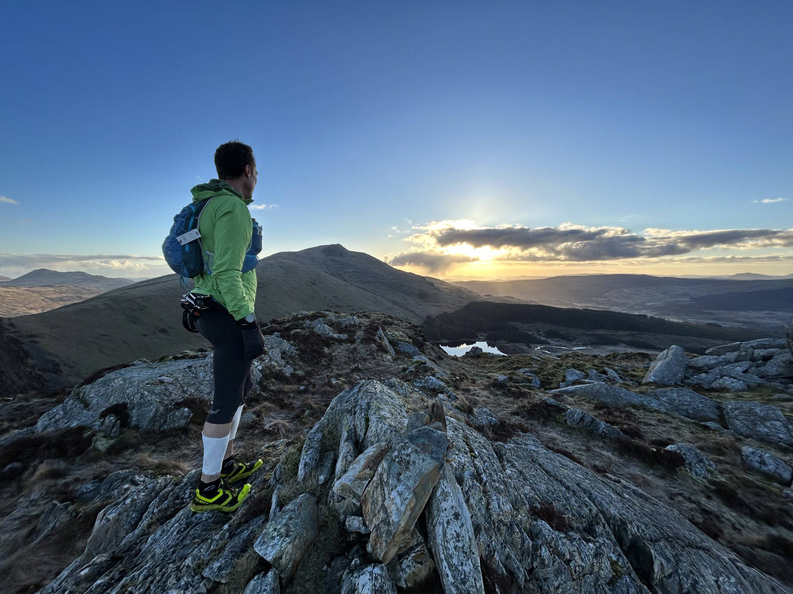 An image of a man look out from the top of a mountain into the sunrise.